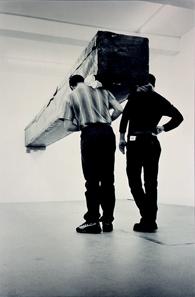 Santiago Sierra, 7 formas de 60x60x600 cm construidas para ser sostenidas en perpendicular a la pared, performance alla Galleria Kilchmann, Zurigo, aprile 2001 (2001; fotografia cromogenica, 230 x 150 cm; Città del Messico, Fundación Jumex)
 Santiago Sierra, 7 formas de 60x60x600 cm construidas para ser sostenidas en perpendicular a la pared, performance alla Galleria Kilchmann, Zurigo, aprile 2001 (2001; fotografia cromogenica, 230 x 150 cm; Città del Messico, Fundación Jumex)
